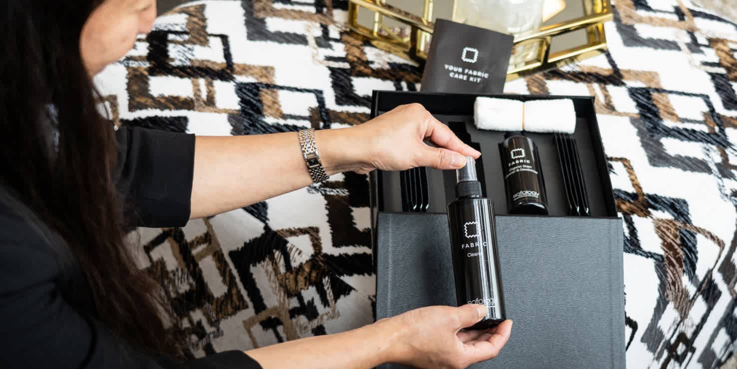 A woman holding a Sofology sofa care kit inspecting one of the cleaning bottles.