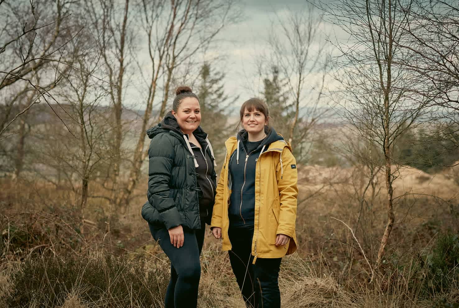 Two people in coats, next to trees