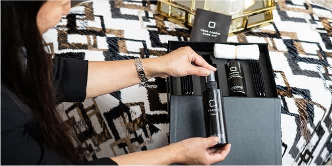 A woman holding a Sofology sofa care kit inspecting one of the cleaning bottles.